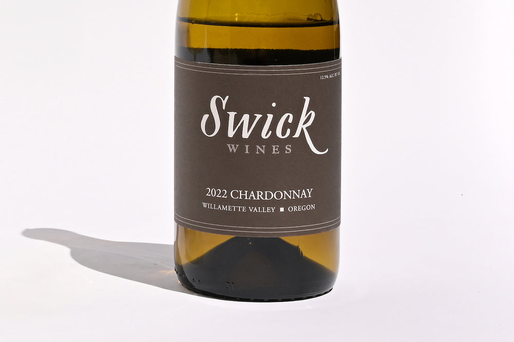 Close-up of Swick Wines 2022 Chardonnay Willamette Valley bottle label with elegant script text on cream and black background on dark green glass
