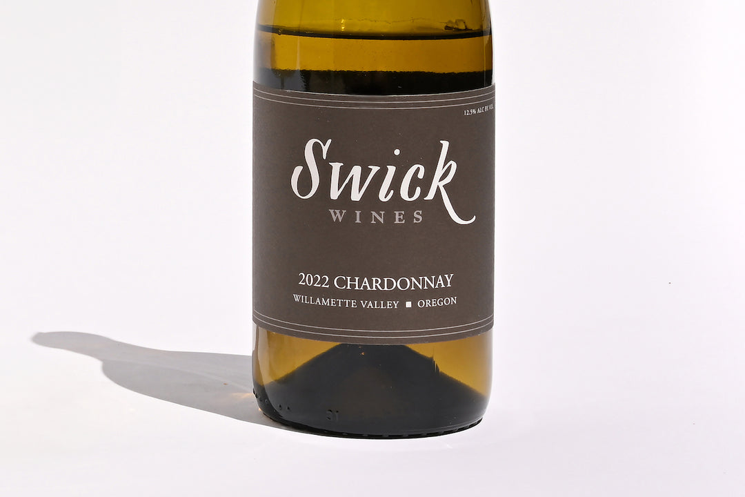 Close-up of Swick Wines 2022 Chardonnay Willamette Valley bottle label with elegant script text on cream and black background on dark green glass