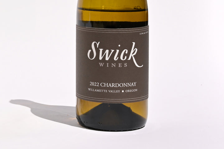 Close-up of Swick Wines 2022 Chardonnay Willamette Valley bottle label with elegant script text on cream and black background on dark green glass