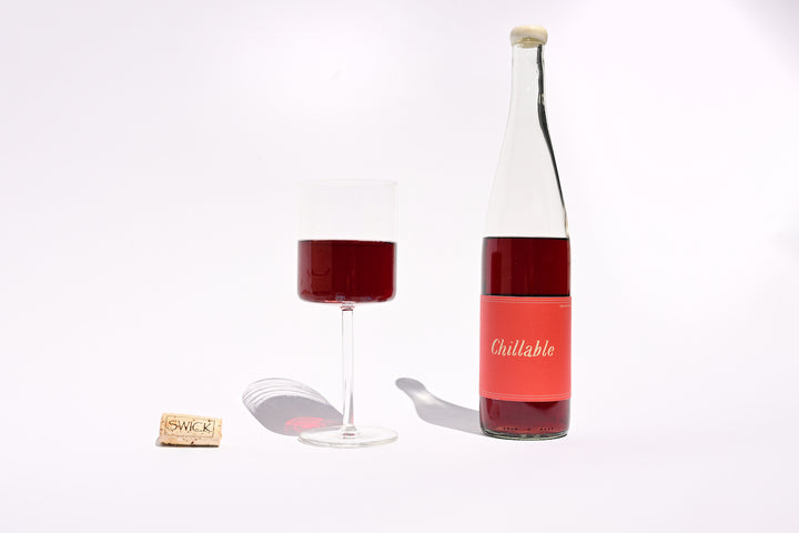 Bottle of Swick Wines 2022 Chillable Red natural wine with a poured glass, showing the bright red-pink color of this Pinot Noir, Pinot Gris, and Grenache Noir blend