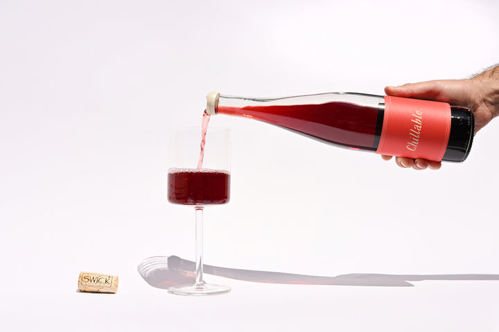Hand pouring Swick Wines 2022 Chillable Red into a wine glass, showing the vibrant red-pink pour of this natural red blend