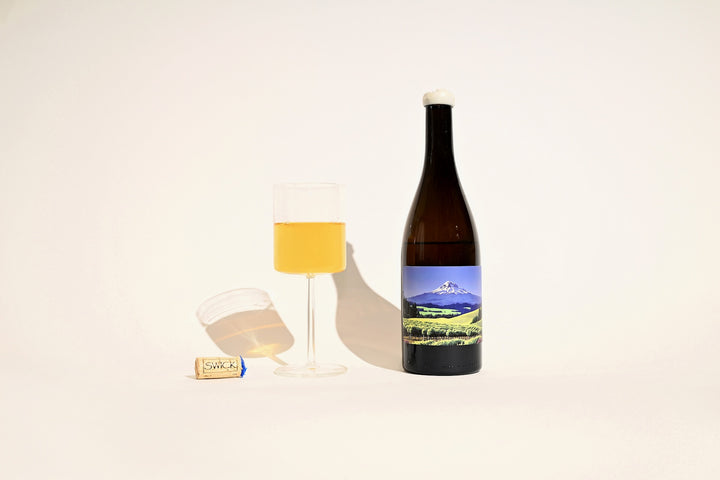 Swick Wines 2022 Gewurztraminer bottle with scenic mountain landscape label, poured glass of golden amber wine, and cork on beige background