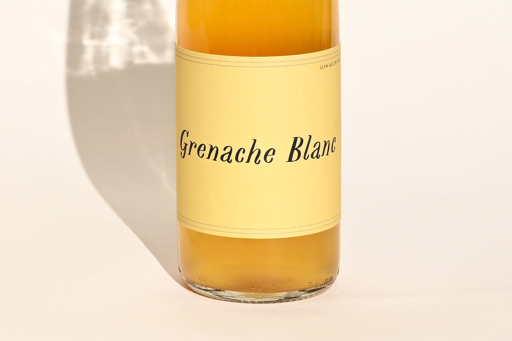 Close-up of Swick Wines 2022 Grenache Blanc bottle label with cursive text on cream background showing golden amber wine through clear glass