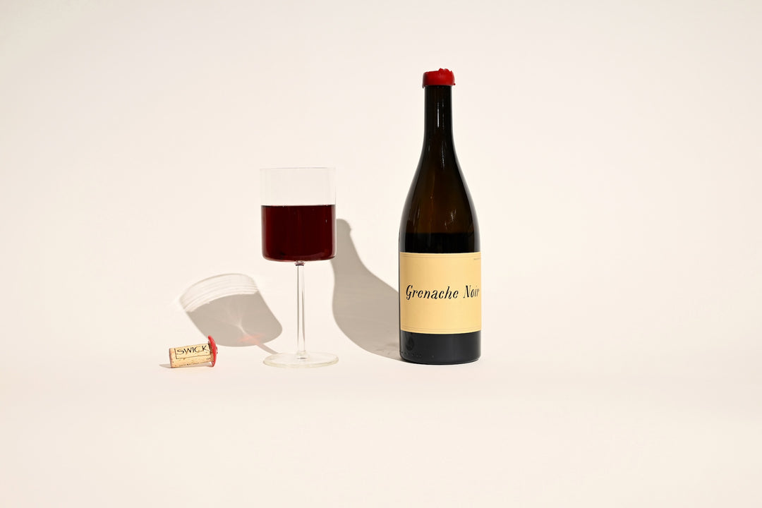 Swick Wines 2022 Grenache Noir bottle with poured glass of red wine and cork on beige background