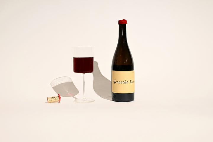 Swick Wines 2022 Grenache Noir bottle with poured glass of red wine and cork on beige background