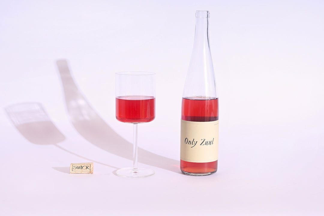 Swick Wines 2023 Only Zuul bottle with cream label and filled glass of vibrant red-pink wine casting shadows on white background