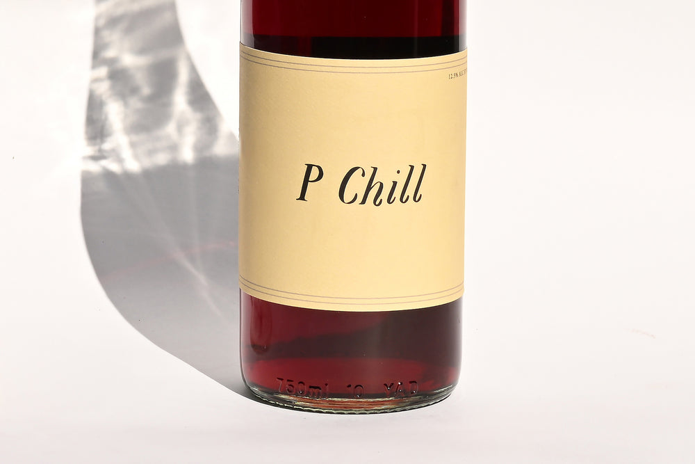 Close-up of Swick Wines 2022 P-Chill bottle label with cursive text on cream background and black upper section showing deep red wine through clear glass