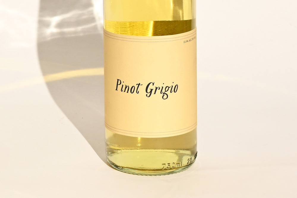 Close-up of Swick Wines 2022 Pinot Grigio bottle label with cursive text on cream background showing pale yellow wine through clear glass