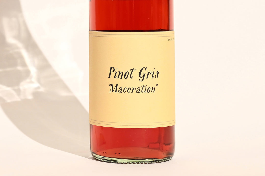 Close-up of Swick Wines 2022 Pinot Gris Maceration bottle label with cursive text on cream background showing red-pink wine through clear glass
