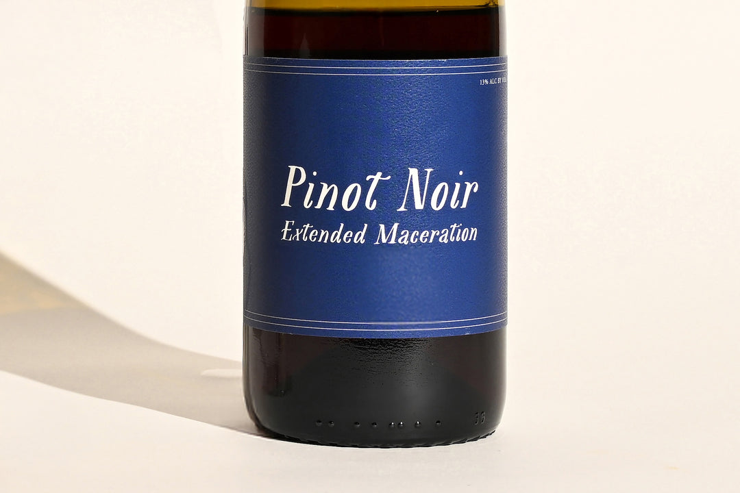 Close-up of Swick Wines 2022 Pinot Noir Extended Maceration blue bottle label with cursive white text on dark green glass