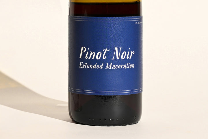 Close-up of Swick Wines 2022 Pinot Noir Extended Maceration blue bottle label with cursive white text on dark green glass
