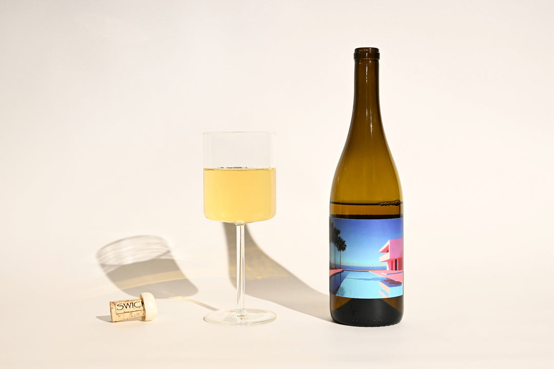 Swick Wines 2022 Poolz #1 bottle with colorful pool and palm tree artwork label, filled glass of pale yellow white wine, and cork on beige background