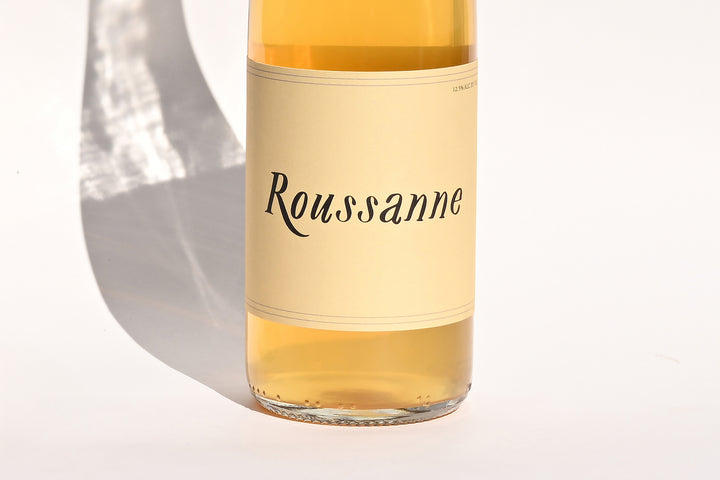 Close-up of Swick Wines 2022 Roussanne bottle label with cursive text on cream background showing golden yellow wine through clear glass