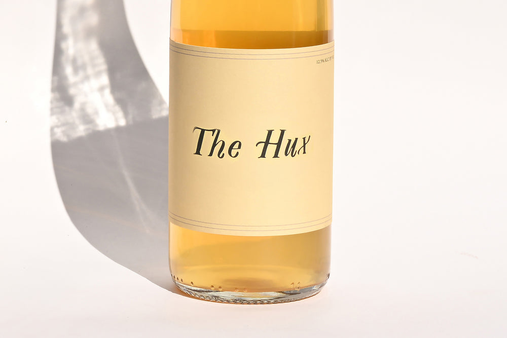 Close-up of Swick Wines 2022 The Hux bottle label with cursive text on cream background showing golden yellow wine through clear glass