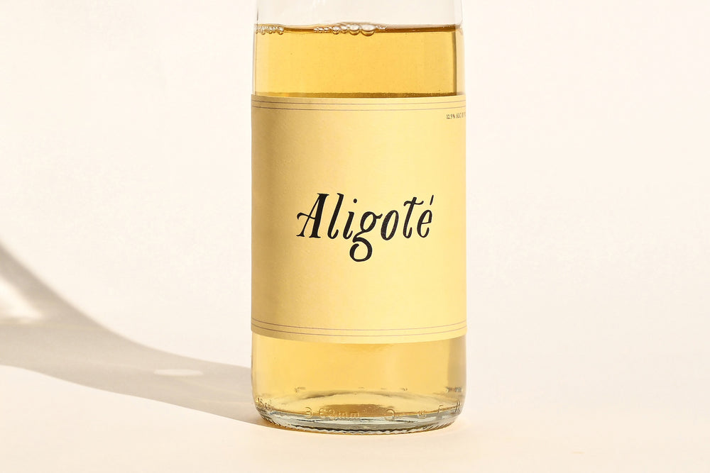 Close-up of Swick Wines 2023 Aligoté bottle label with cursive text on cream background showing pale gold white wine through clear glass