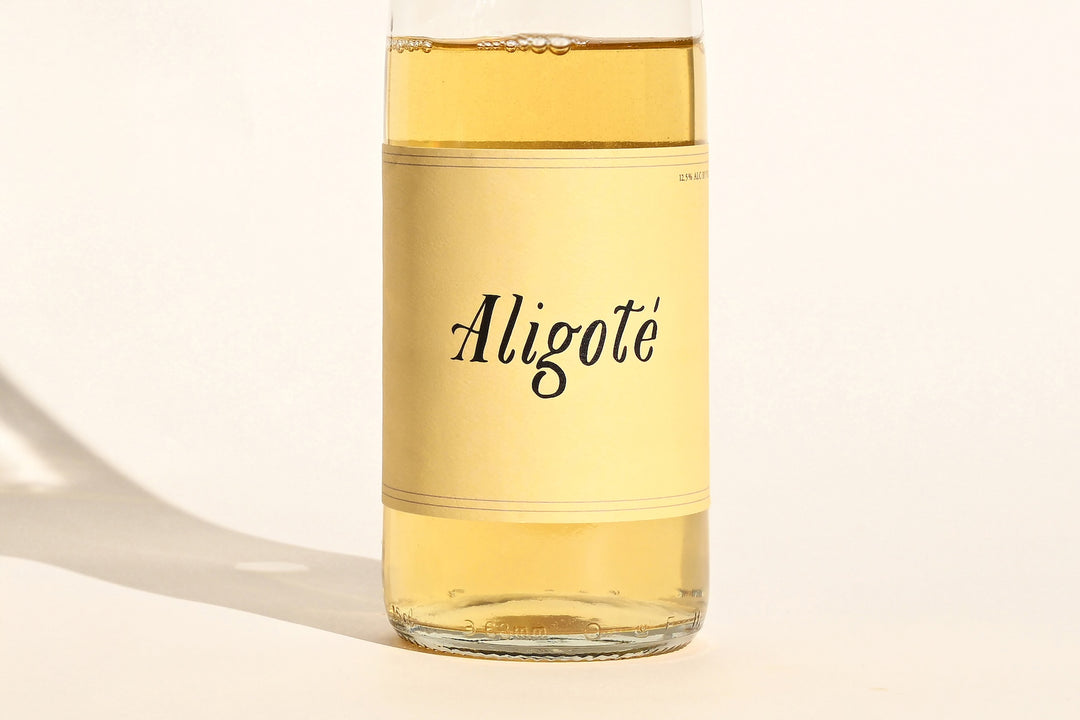 Close-up of Swick Wines 2023 Aligoté bottle label with cursive text on cream background showing pale gold white wine through clear glass