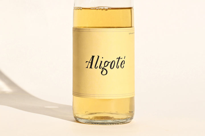 Close-up of Swick Wines 2023 Aligoté bottle label with cursive text on cream background showing pale gold white wine through clear glass
