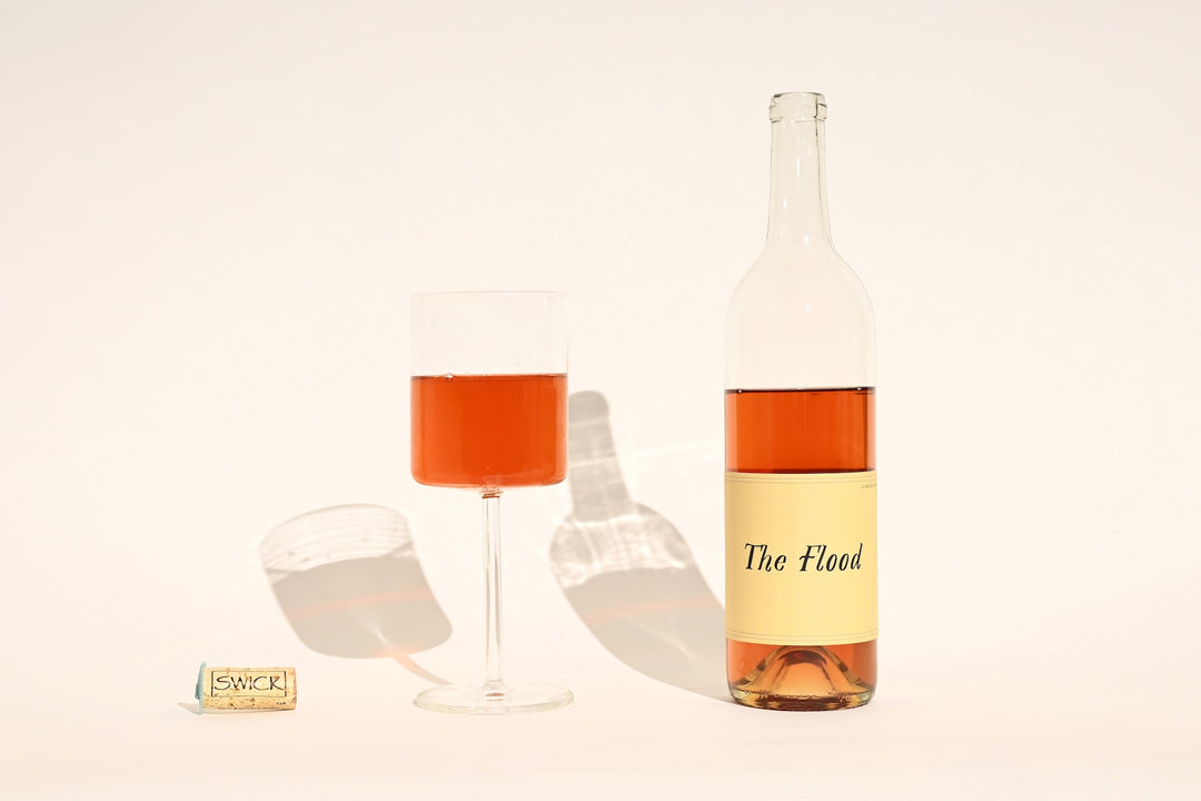 Swick Wines 2023 The Flood bottle with peach-orange rosé wine, filled glass, and cork on beige background