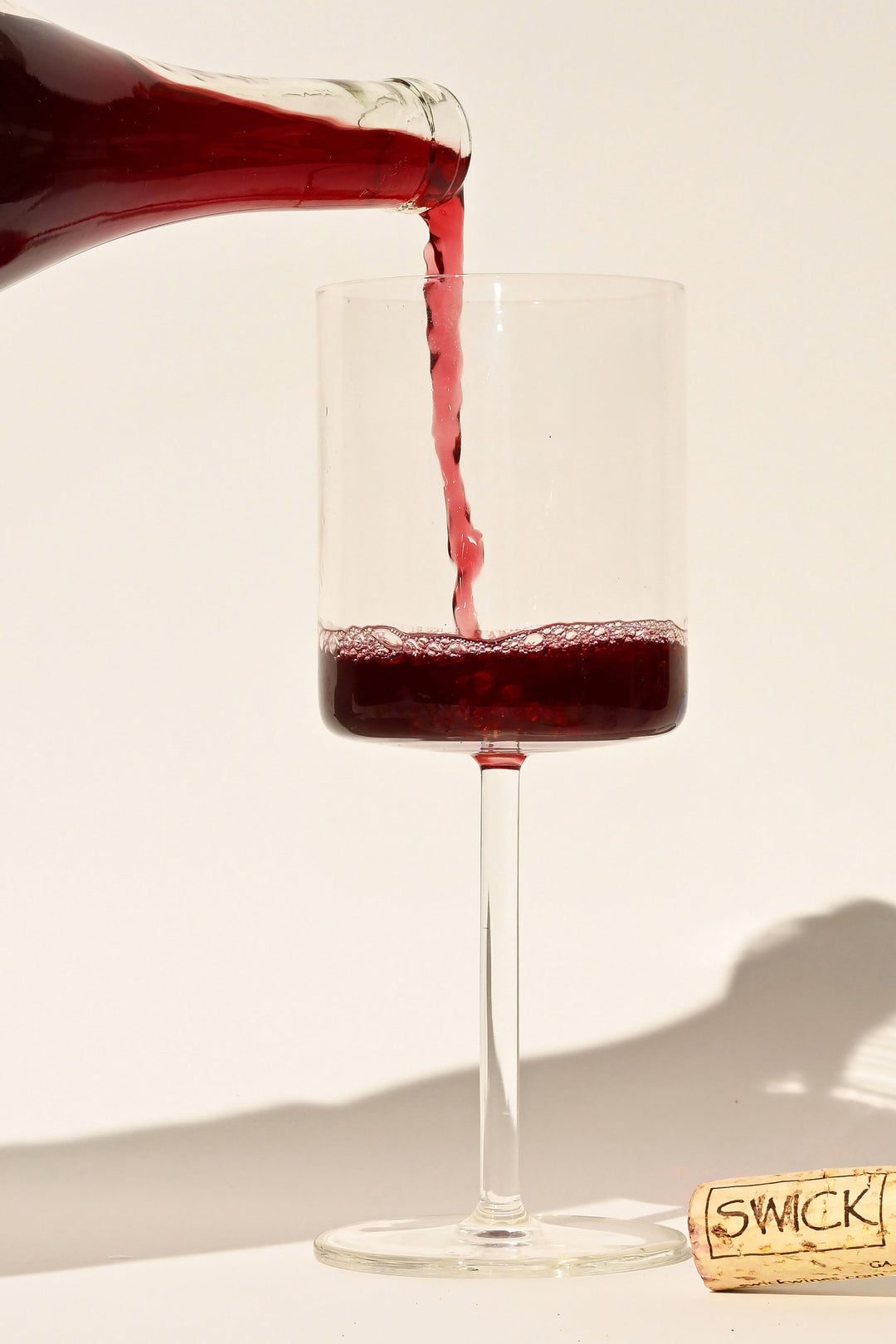 Swick Wines Raw Reds sampler deep red wine being poured from bottle into a glass with Swick branded cork on beige background