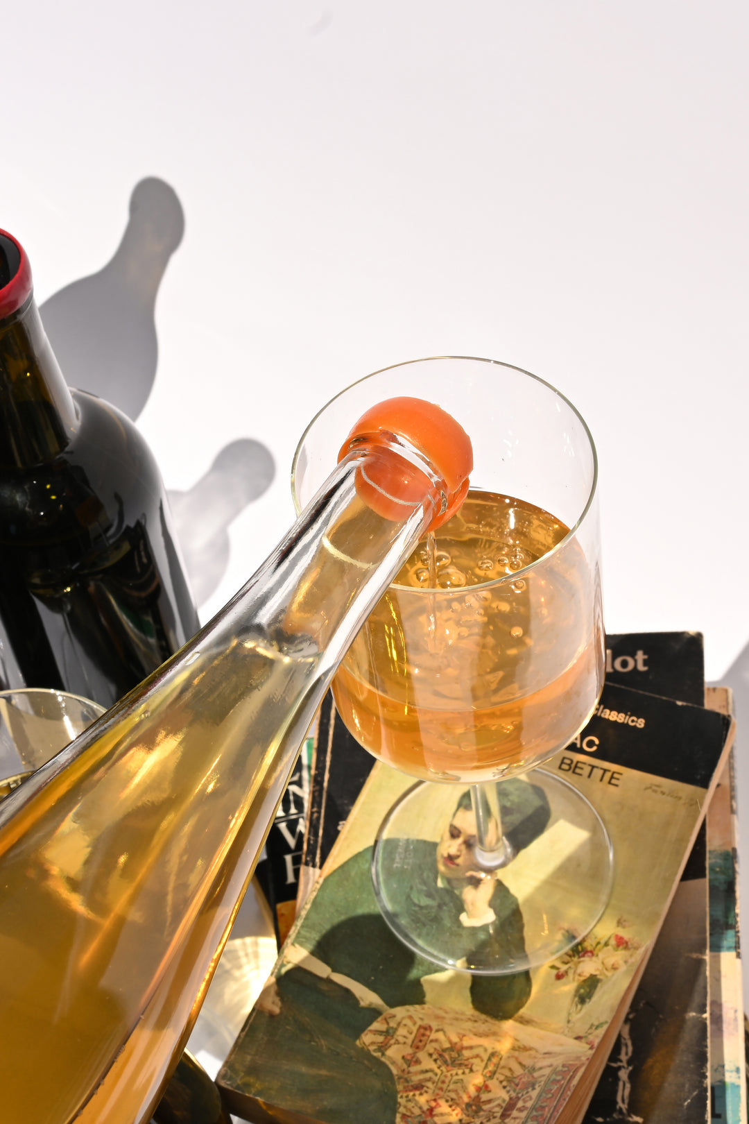 Swick Wines Skin Contact Sampler amber orange wine being poured from bottle into a glass with wine bottles and books on a sunlit table